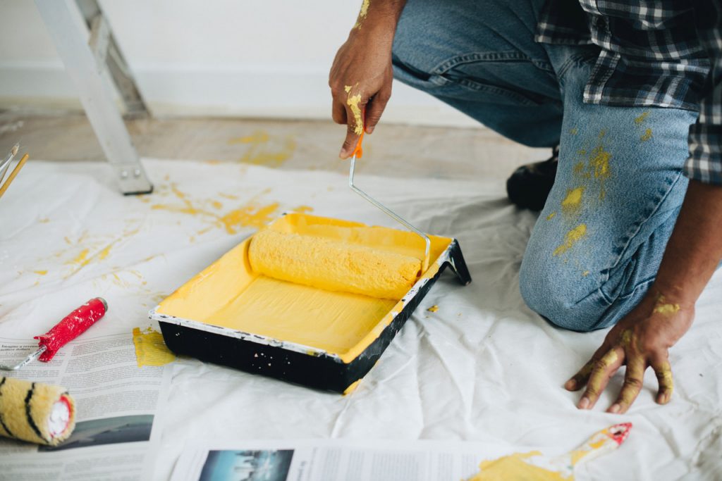 home contractor with roller in yellow paint, some spilled on floor